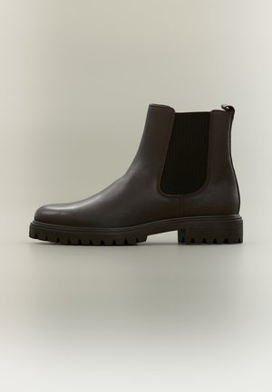 Bottine Chelsea en cuir marron foncé avec panneaux latéraux élastiques noirs et semelle robuste sur fond neutre.