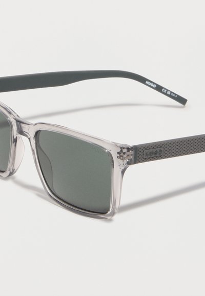 Lunettes de soleil carrées à verres foncés avec montures avant transparentes et branches noires texturées embossées du logo "HUGO".