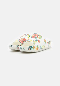 Des chaussures à enfiler à motif floral avec une base blanche ornée de fleurs multicolores, des bouts ronds et des semelles en caoutchouc texturé pour une meilleure adhérence.