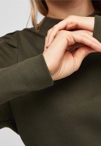 Oliwkowa koszula z długim rękawem, z prążkowanymi mankietami i luźnym krojem, charakteryzująca się gładką fakturą materiału i minimalistycznym designem.