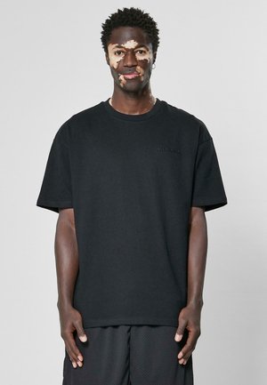 Schwarz Baumwoll-T-Shirt mit runder Halslinie, kurzen Ärmeln und lockerem Schnitt, das ein dezentes gesticktes Logo auf der Brust hat.