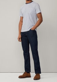 Striped short-sleeve shirt in white and navy, dark denim jeans, and brown suede shoes. Relaxed fit with standard collar and pockets.