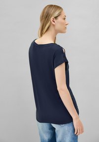 Haut à manches courtes bleu marine avec des détails découpés aux épaules, en tissu doux, coupe ample et décolleté arrondi, associé à un jean bleu clair.