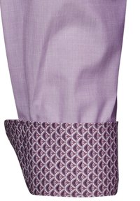 Cuff di camicia di un leggero viola con una fodera interna a motivo che presenta un design a onde ripetuto in viola scuro e accenti bianchi.