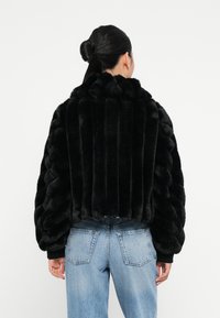 Sort faux fur jakke med vertikale og horisontale striber, med oversized ærmer og ribbede manchetter, parret med lyseblå jeans.