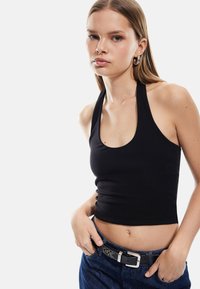 Svart halterneck-top i stretchtyg med rundad halsringning. Matchad med blå jeans och ett svart spännbälte.