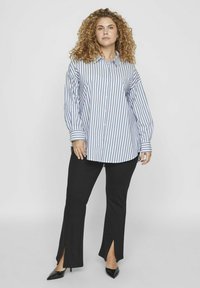 Camisa de botones a rayas en azul y blanco, combinada con pantalones negros con cortes laterales, complementada con tacones negros puntiagudos.