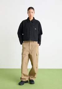 Zwart cropped jack met een ritssluitingen, zijzakken en logo patch. Gecombineerd met khaki cargo pants met meerdere zakken en een relaxte pasvorm.