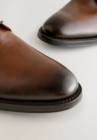 Brown leather shoes with a polished finish, featuring rounded toes and detailed stitching along the sole. Smooth texture and classic design.