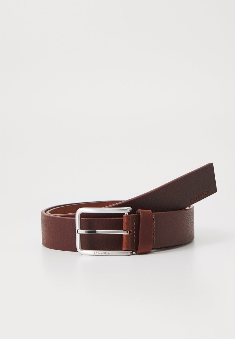 Ceinture en cuir marron avec une texture lisse, boucle rectangulaire en argent, et une étiquette affichant "Calvin Klein." Design simple et moderne.