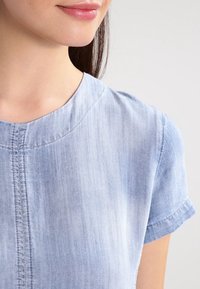 Vaaleansininen, lyhythihainen paita pyöreällä kaula-aukolla, joka on valmistettu pehmeästä kankaasta. Paidassa on hienovarainen tekstuuri ja keskiraita.