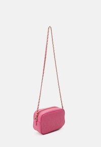 Sac bandoulière rose avec un logo embossé, de forme rectangulaire, et une chaîne dorée. Texture douce avec fermeture éclair.