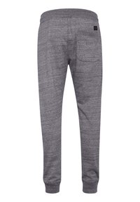 Pantalones de chándal grises con una tela texturizada, cinturilla elástica y puños, que cuentan con un solo bolsillo trasero y una pequeña etiqueta de la marca.
