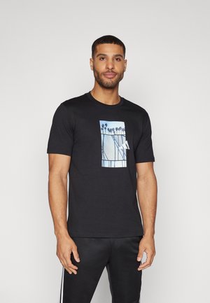 T-shirt noir en coton avec un motif graphique bleu clair de palmiers sur un fond géométrique. Encolure ronde, manches courtes.