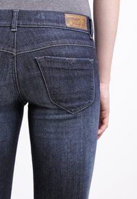 Jeans in denim blu scuro con vestibilità slim, dotati di una tasca posteriore e di un'etichetta in pelle sulla cintura. Tessuto liscio.