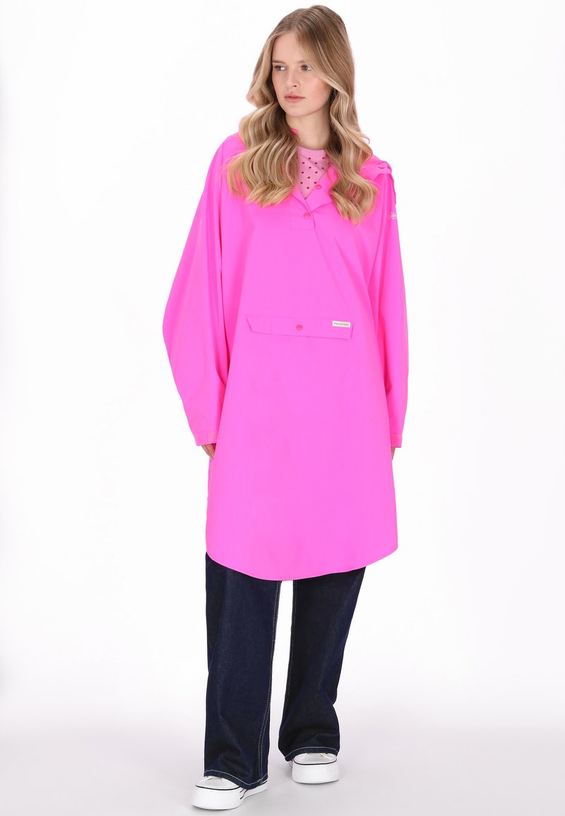 Rózsaszín vízálló dzseki laza szabással, elülső zsebbel és kapucnival. Sötét farmernadrágra és fehér tornacipőre viselve.