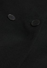 Tissu en laine noire avec deux boutons ronds noirs cousus, montrant la texture et les détails des boutonnières.