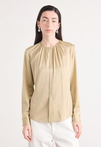 Blusa beige a maniche lunghe con scollo arricciato, pieghe frontali e polsini con bottoni. Tessuto liscio, vestibilità tailored.