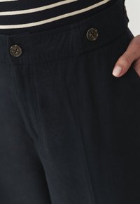 Navyblauwe broek met een gladde textuur, voorzien van een platte tailleband, twee grote bruine knopen en gestreken voorplooien.