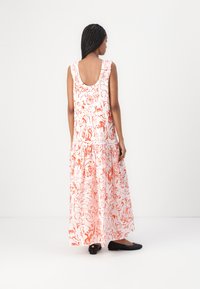 Maxikleid aus leicht rosa Stoff mit roten Blumenmustern, ärmelloses Design, runder Ausschnitt hinten und mehrlagigem Rüschensaum. Kombiniert mit schwarzen Ballerinas.
