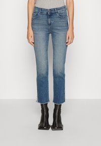 Modré džínové kalhoty s rovnými nohavicemi, roztrhaným lemem a bočními pruhy. Nosené s černými kotníkovými botami se čtveratou špičkou. Hladká textura.