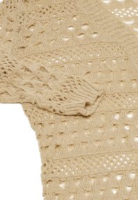 Maglione lavorato a maglia in beige chiaro con un design a traforo caratterizzato da motivi a rombo, polsini a coste e filato testurizzato.