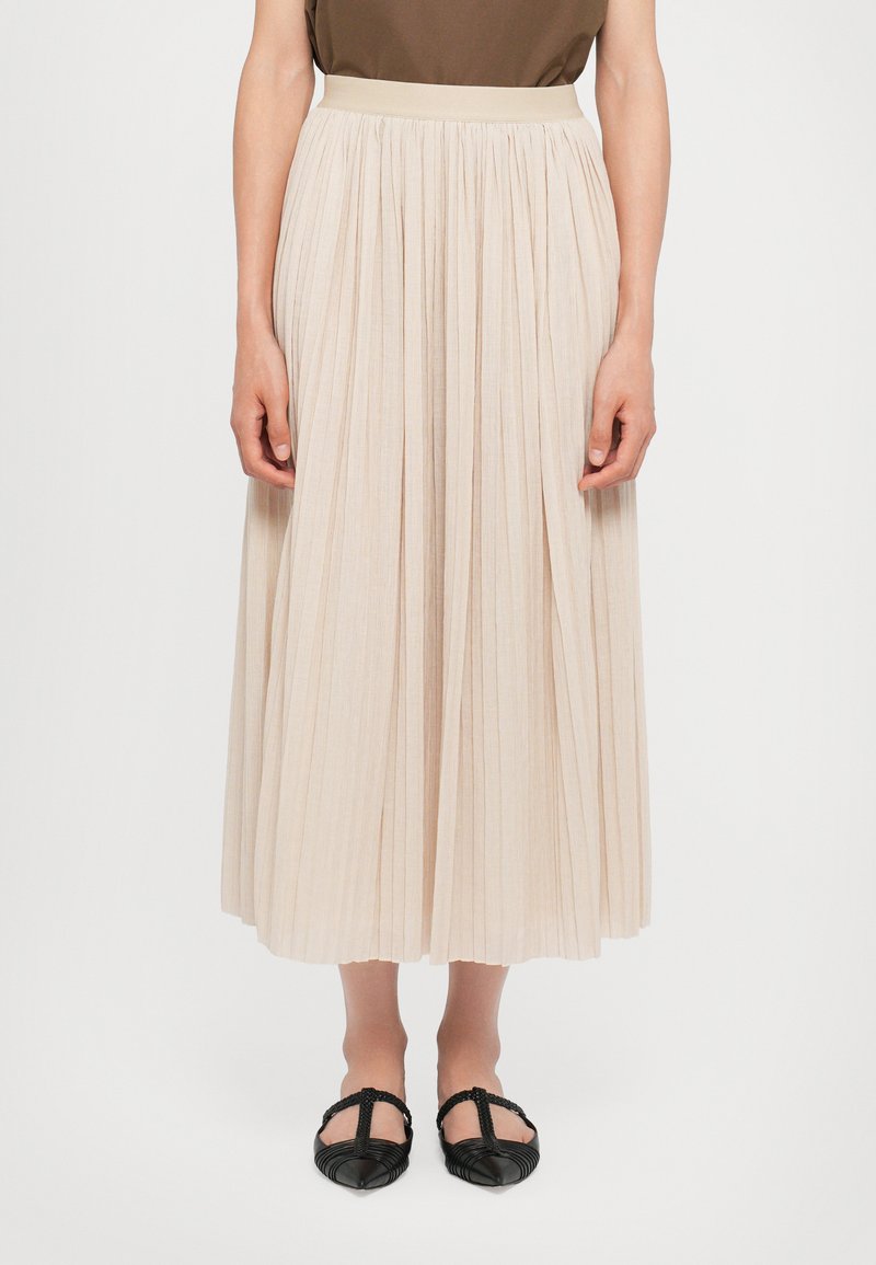 Faltenrock in hellem Beige, ausgestattet mit einem elastischen Bund, weicher Textur und fließendem Design, kombiniert mit schwarzen flachen Schuhen.
