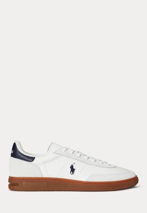 Lavtop hvid lædersneaker med brun sål, marineblåt hæl-detalje, snørebånd og en marineblå polospiller-logo på siden.