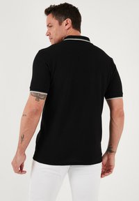 Černé polo tričko s texturovanou vazbou, s šedými akcenty na límci a lemech rukávů. Klasický střih s postranními rozparky na lemu.