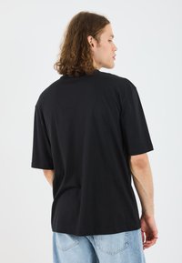 Svart bomulls t-skjorte med avslappet passform, korte ermer, rund hals, og ensfarget bak. Kombinert med lyseblå denimjeans.