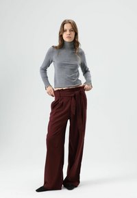 Grijze coltrui gecombineerd met hooggesneden bordeauxrode broek met ceintuur, losse pasvorm en brede pijpen, met een gladde textuur.