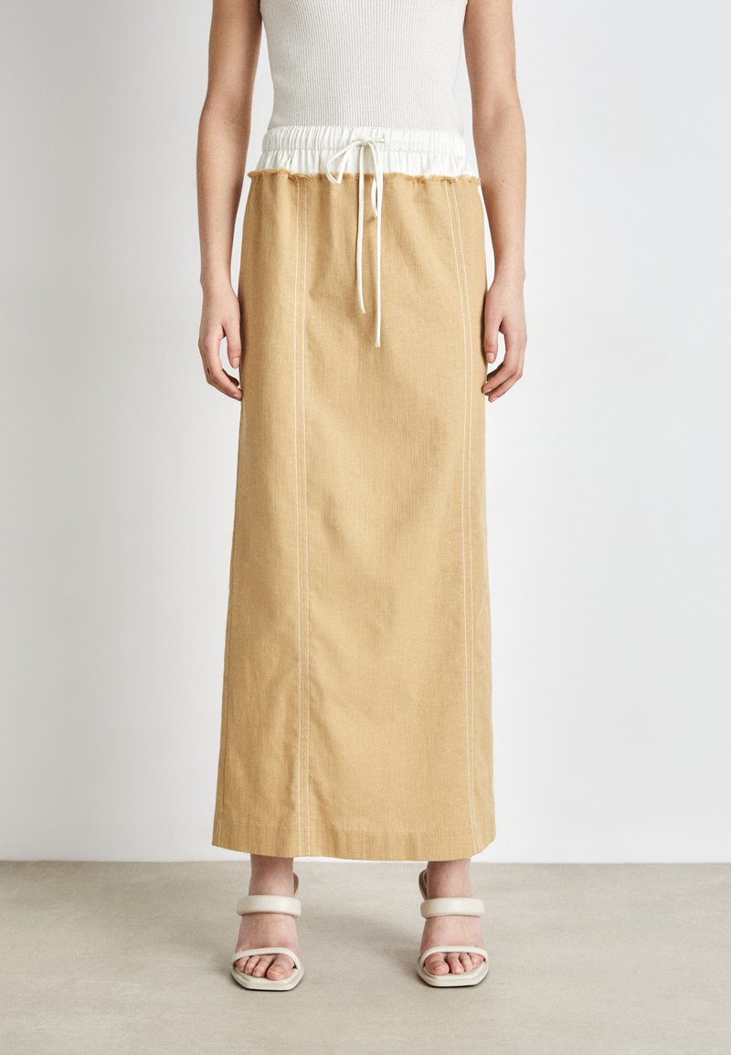 Lang, beige nederdel med hvid elastisk talje og snor. Har lige snit, sidesømme og et subtilt struktureret stof.