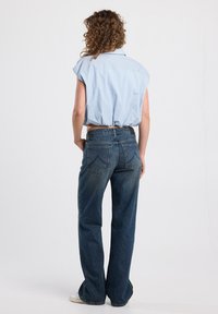 Sininen ja valkoinen raidoitettu lyhythihainen paita, korkeavyötäröiset siniset suorat farkut, vaaleat, joissa on nappi- ja taskuyksityiskohtia.