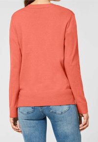 Korallfärgad stickad tröja med rund halsringning och långa ärmar, med ribbade muddar och nederkant. Bärs tillsammans med blå denimjeans.