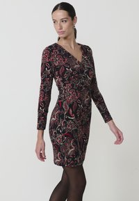 Vestido negro con un patrón floral en rojo y dorado, con mangas largas y un diseño de escote en V. Corte ajustado, tela texturizada.