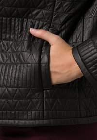 Svart quiltad läderjacka med ett texturerat diamantmönster, med en sidoficka och texturerade ärmslut, som framhäver den släta ytan.