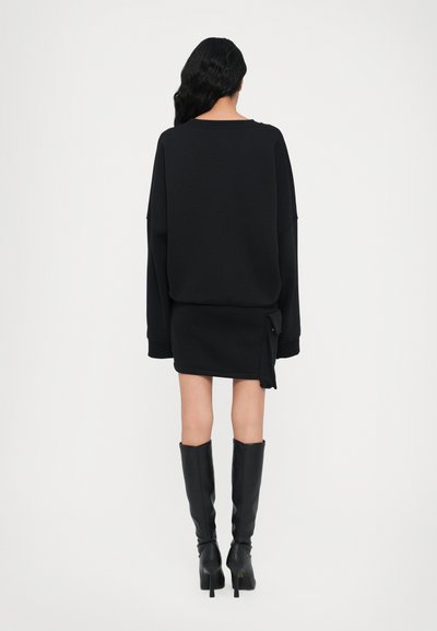 Must be beebi musta oversize-sweater koos musta mini-seeliku ja kõrge kontsaga mustade sääristega nahkkingadega, millel on seeliku külgdetail.