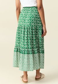 Groene maxi rok met een gelaagd ontwerp. Voorzien van een bloemenprint en contrasterende horizontale strepen aan de zoom. Gemaakt van lichte stof.