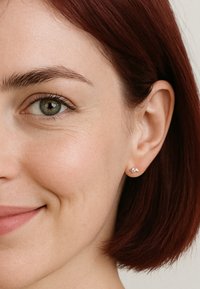 Boucles d'oreilles en argent avec un design courbé simple, portées sur des cheveux châtains courts, mettant en valeur une peau lisse et un look naturel.