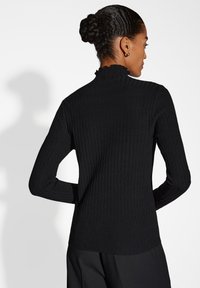 Pull à col roulé noir à côtes avec une finition texturée, doté d'un col rufflé et de manches longues, associé à un pantalon noir ajusté.