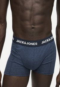 Αρσενικός κορμός με μπλε εσώρουχο Jack & Jones με ελαστική μέση με λογότυπο, που δείχνει μυώδη κοιλιά και χέρια.