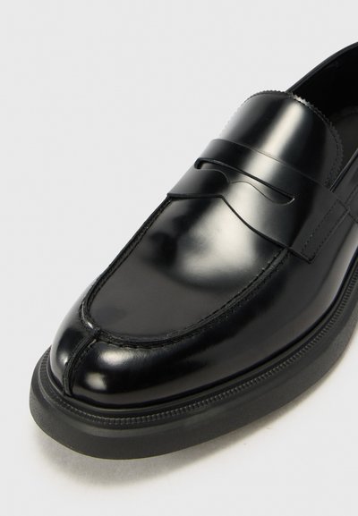 Mocasini din piele neagră, cu un finisaj neted, detalii cusute și o curea decorativă peste părțile din față; dotati cu o talpă groasă din cauciuc.