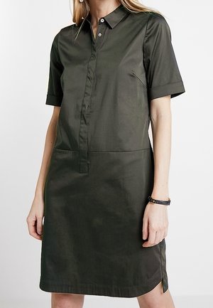 Sukienka z krótkim rękawem w ciemnozielonym kolorze, wykonana z gładkiej tkaniny. Posiada kołnierzyk, zapinana na guziki z przodu oraz ma boczne rozcięcia, które ułatwiają ruch.