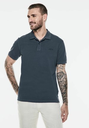 Dunkelblaues Poloshirt aus Baumwollmischung mit einer Druckknopfverschlussleiste und gesticktem Logo. Kurze Ärmel, glatte Textur, kombiniert mit hellen Hosen.