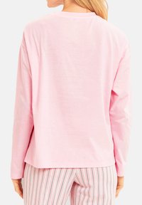 Långärmad rosa skjorta med avslappnad passform, slät textur och rund halsringning; matchad med randiga pyjamasbyxor i ljusare rosa och vitt.