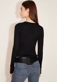 Schwarzes geripptes Langarmshirt mit rundem Ausschnitt, kombiniert mit blauen Jeans, die an der Taille mit schwarzem Leder akzentuiert sind.