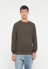 Suéter de punto texturizado de color gris oscuro con cuello redondo, puños acanalados y dobladillo. Llevado con jeans de color azul claro frente a un fondo blanco liso.