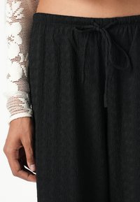 Zwarte textuur broek met een koord taille. Ze hebben een zachte, golvende stof en een relaxte pasvorm voor comfort en vrijheid van beweging.