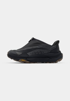 Sort slip-on sko med en tekstureret overdela, glatte detaljer, gummisål med mønster og et gult Vibram-logo på ydersålen.