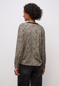 Beżowa bluzka w czarne kropki, z długim rękawem i czarnym kołnierzykiem, zestawiona z ciemnymi dżinsami, widok od tyłu.